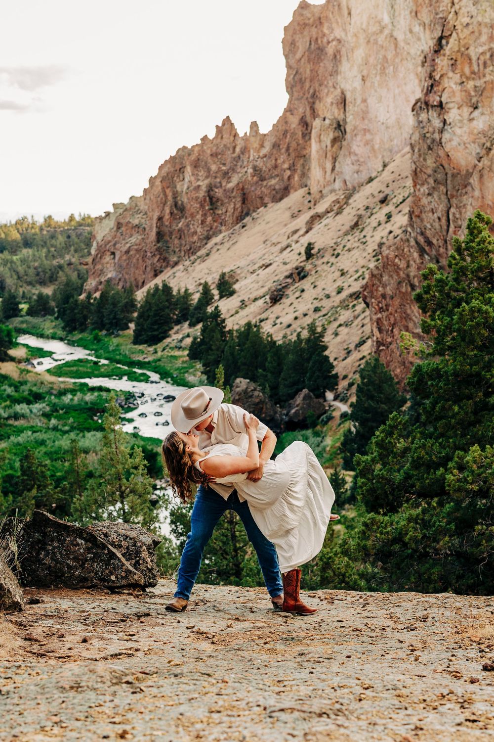A romantic moment against the stunning backdrop of Smith Rock State Park with towering cliffs and winding river below.