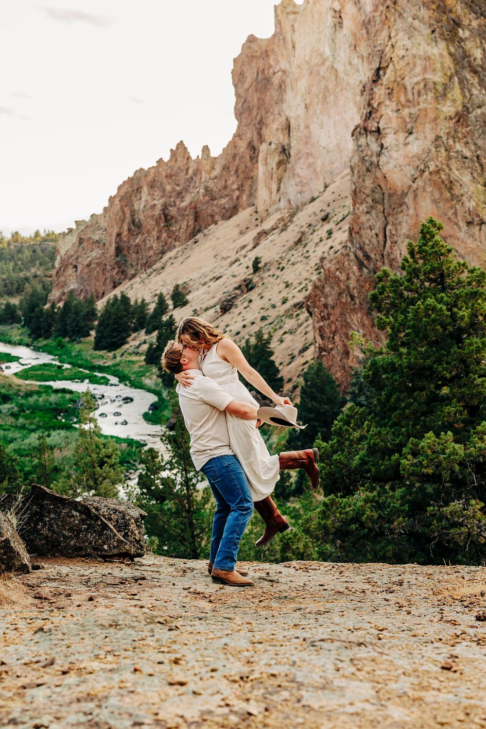 Playful dance lift pose photographed along scenic canyon overlook with river and cliffs in background.