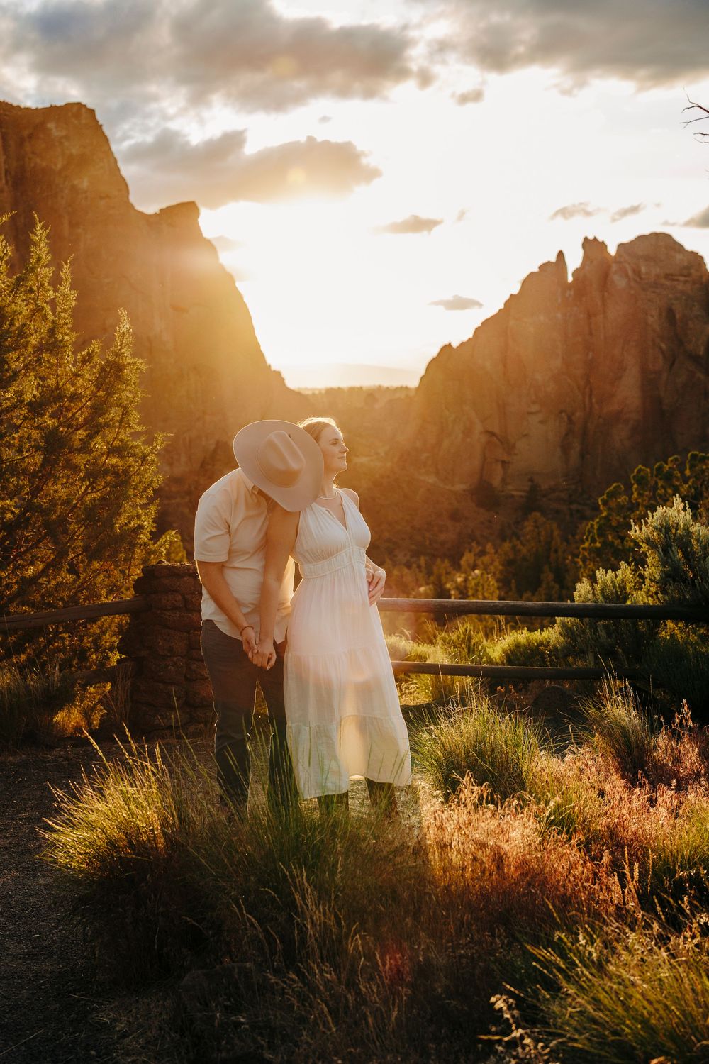 A romantic sunset silhouettes towering red rock cliffs at Smith Rock State Park as couple shares intimate moment in golden light.