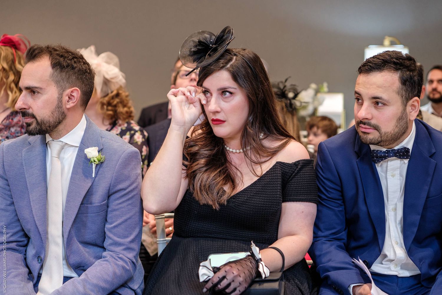 Wedding guests watch ceremony with emotional expressions while seated in formal attire.