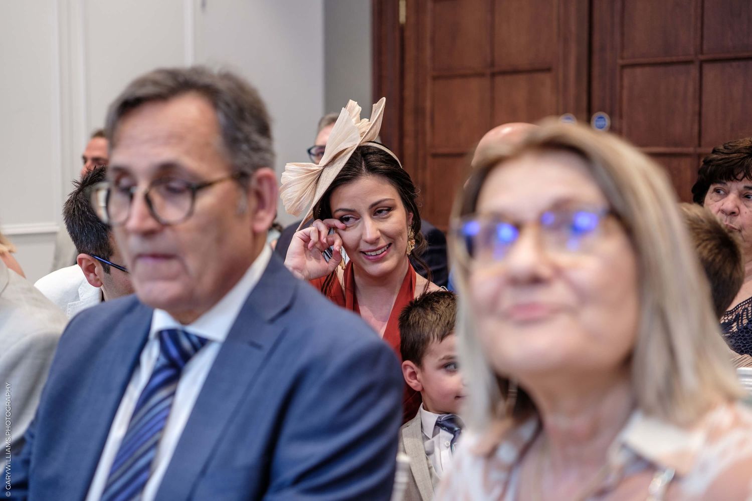 People sitting together during an event with someone visibly peering and smiling from between them in the background.