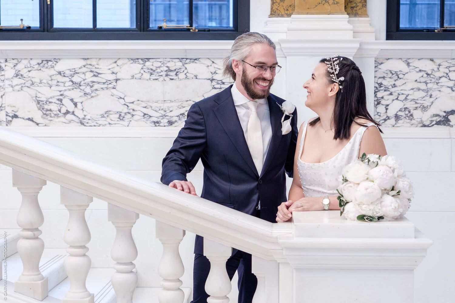 Happy couple sharing a joyful moment together on a grand marble staircase during their outdoor wedding photoshoot.