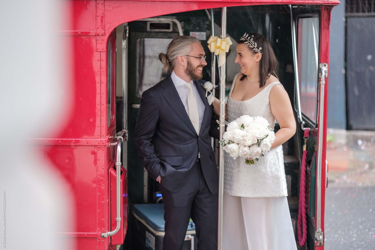 A couple emerges from a red door on their wedding day with the bride wearing a white dress and holding a bouquet.