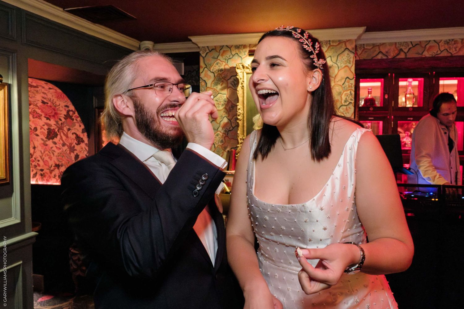 Two people sharing an animated moment of laughter together at a dimly lit venue with red decor in the background.