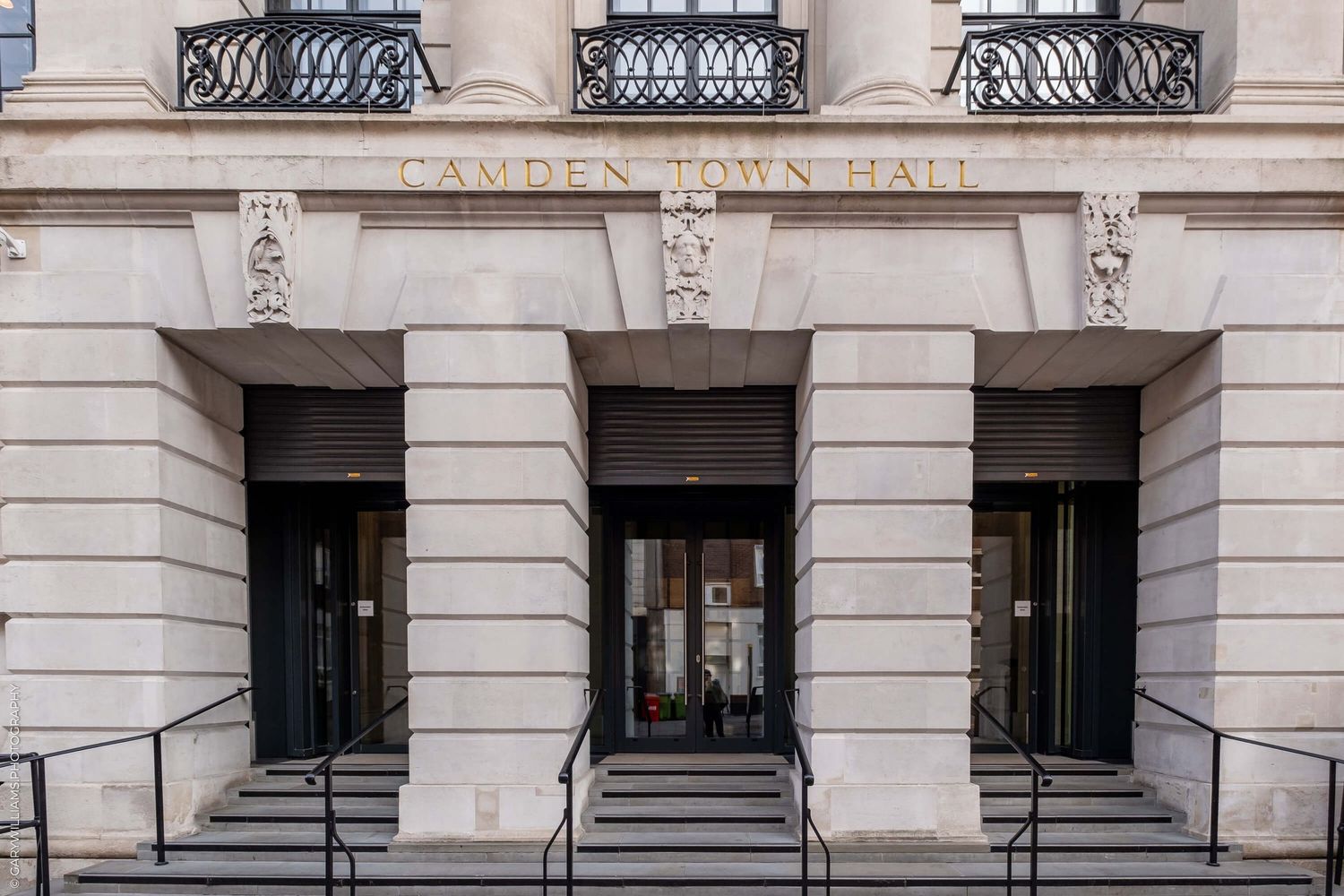 Historic stone building facade with ornate wrought iron railings and multiple entrance doorways and stairs.