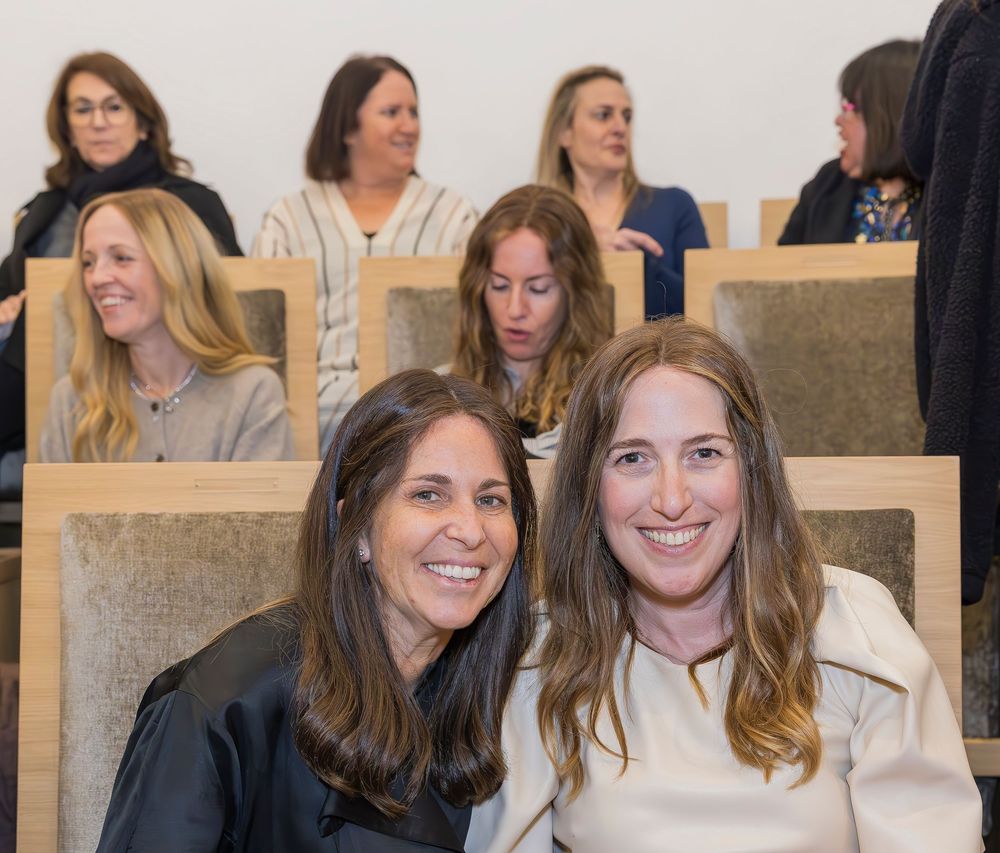 People sitting in rows of auditorium seating at an indoor event, smiling and engaged.