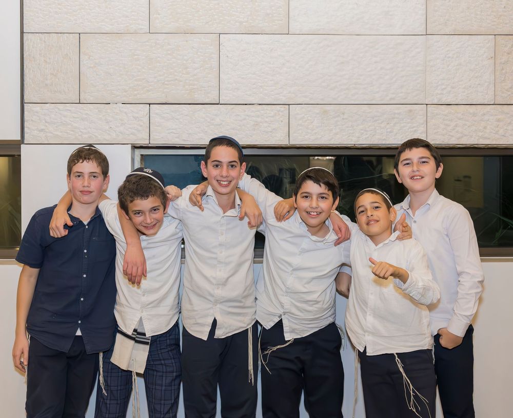 A group of six friends in casual attire standing together and posing against a brick wall outdoors.