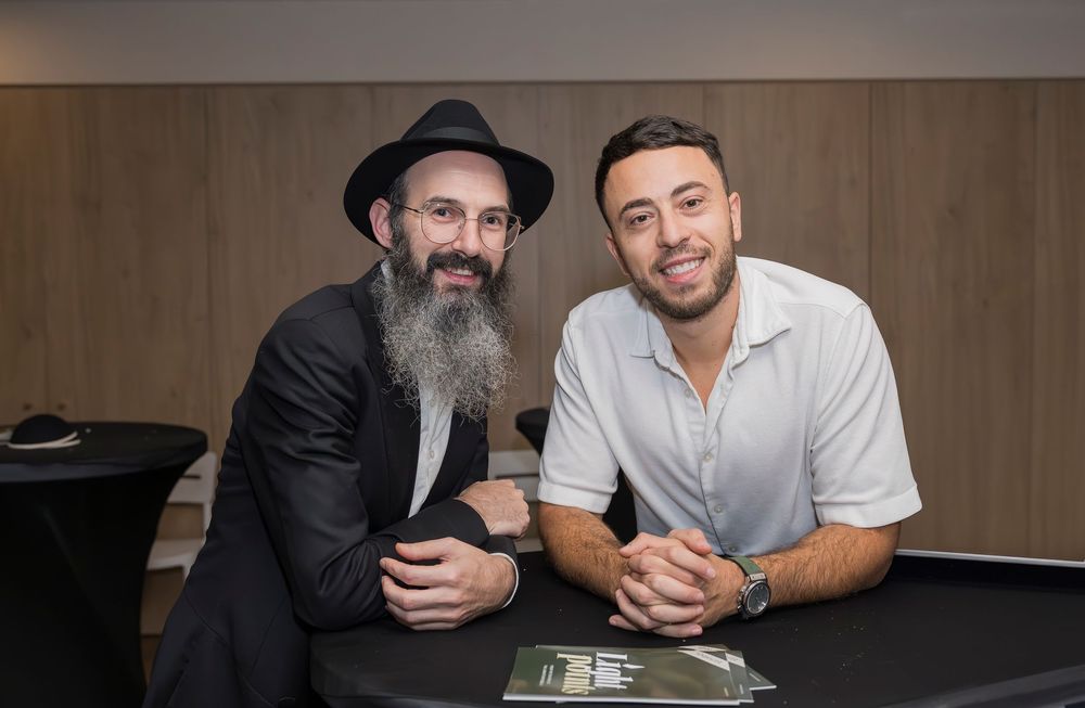 Two people sitting at a table smiling and signing documents in a casual office setting.