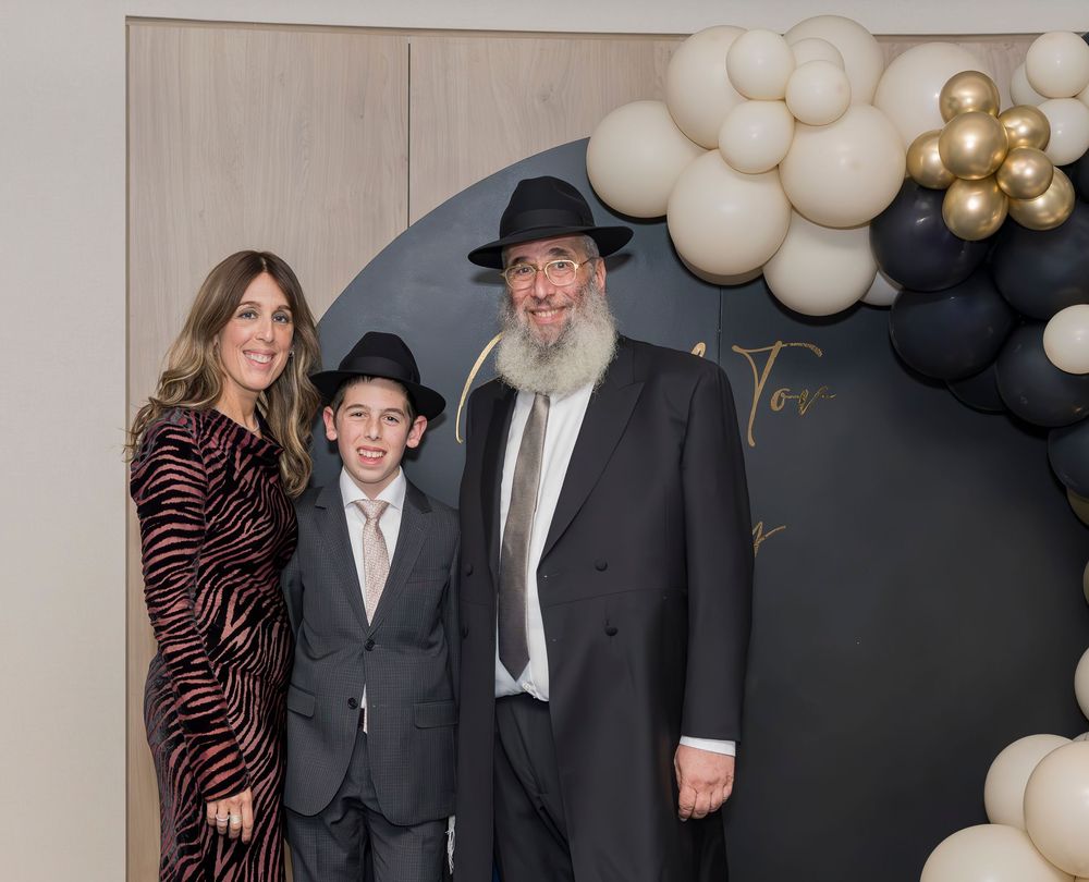 People stand together against a dark backdrop with gold and white balloon decorations at a formal event.