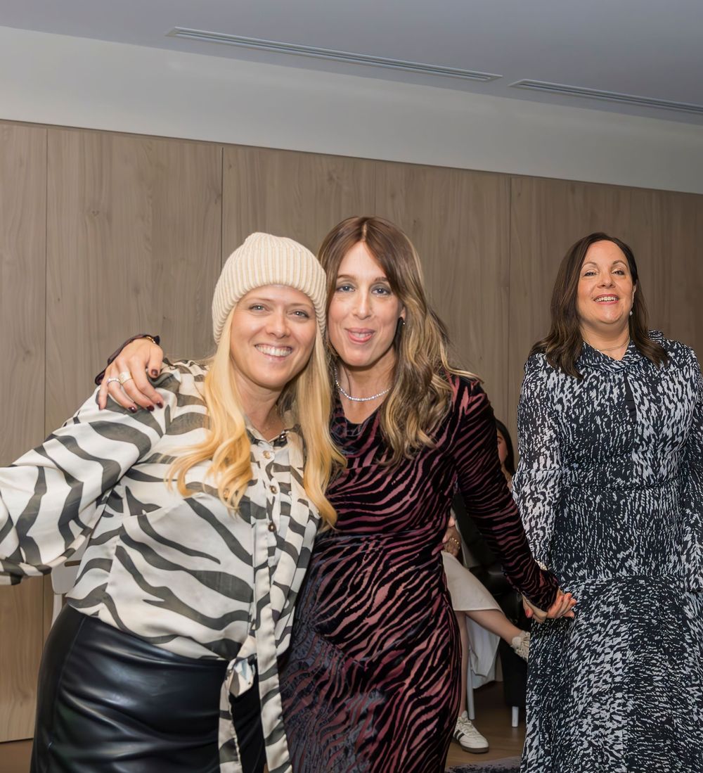Three people wearing animal print and dark clothing pose together at an indoor event.