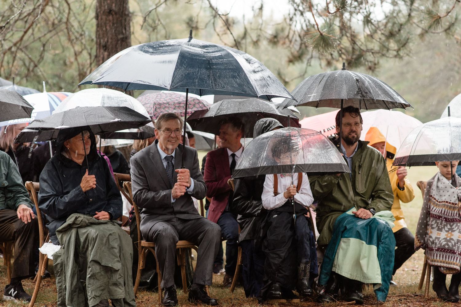 A group of people huddle under umbrellas during outdoor event in rainy weather.
