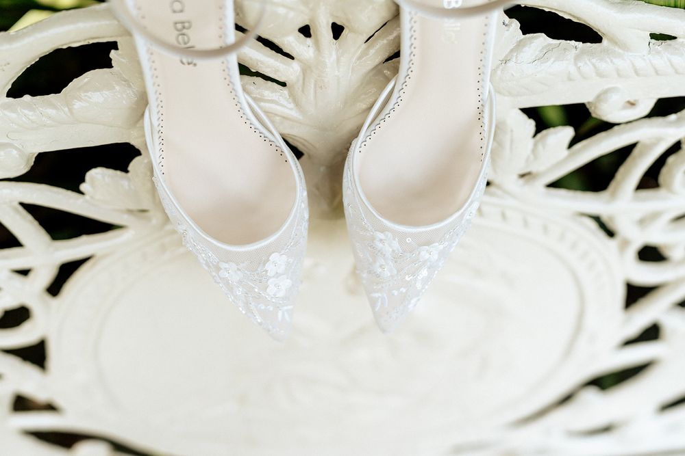 Elegant white leather bridal shoes and jewelry arranged on white lace background.