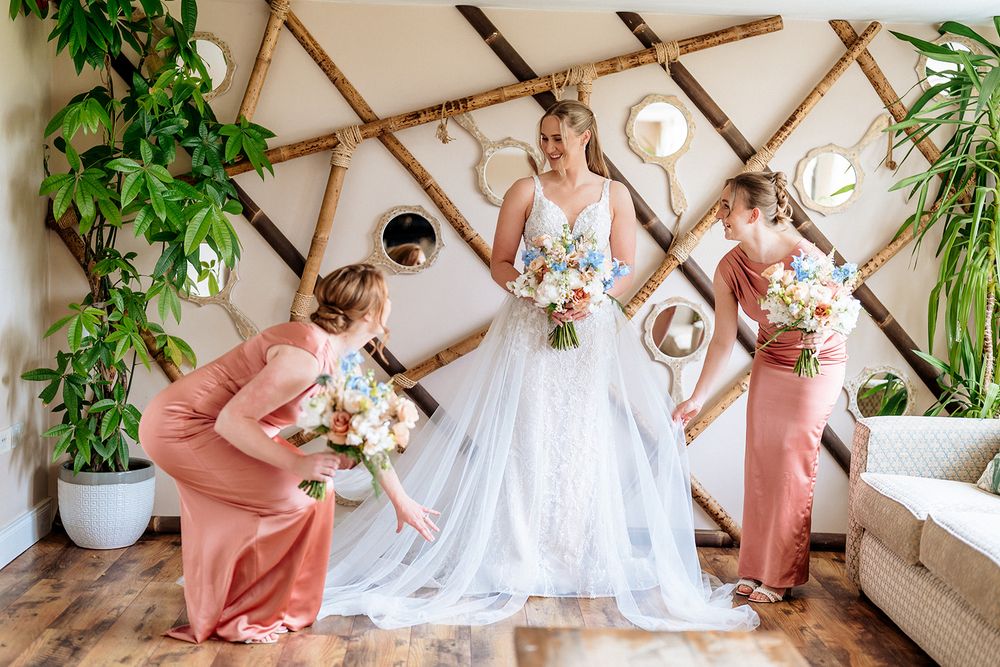 Bridal party poses joyfully in front of wooden lattice wall with greenery and flowers during wedding celebration.