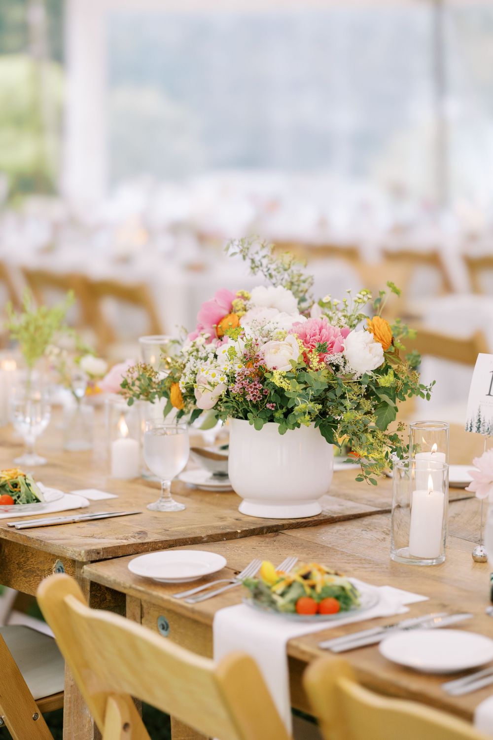 Elegant wedding centerpiece with pink and white flowers in white vase on rustic farm table with place settings.