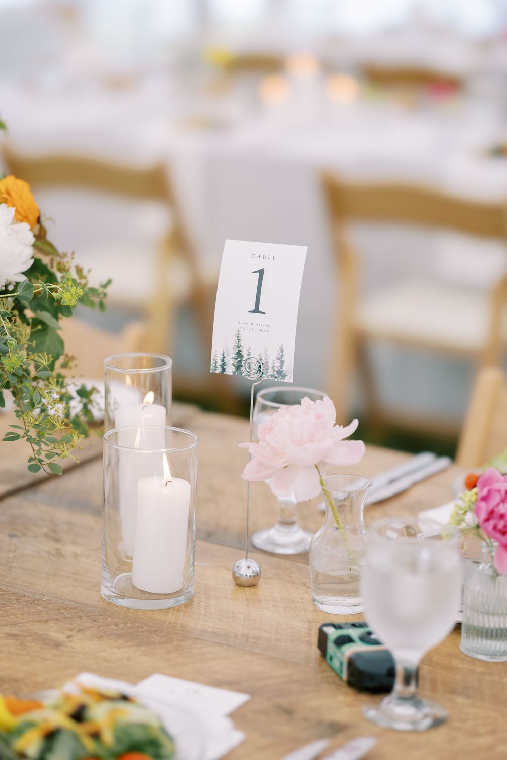 Wedding reception table setting with table number 1, candles, and delicate floral accents on rustic wooden table.