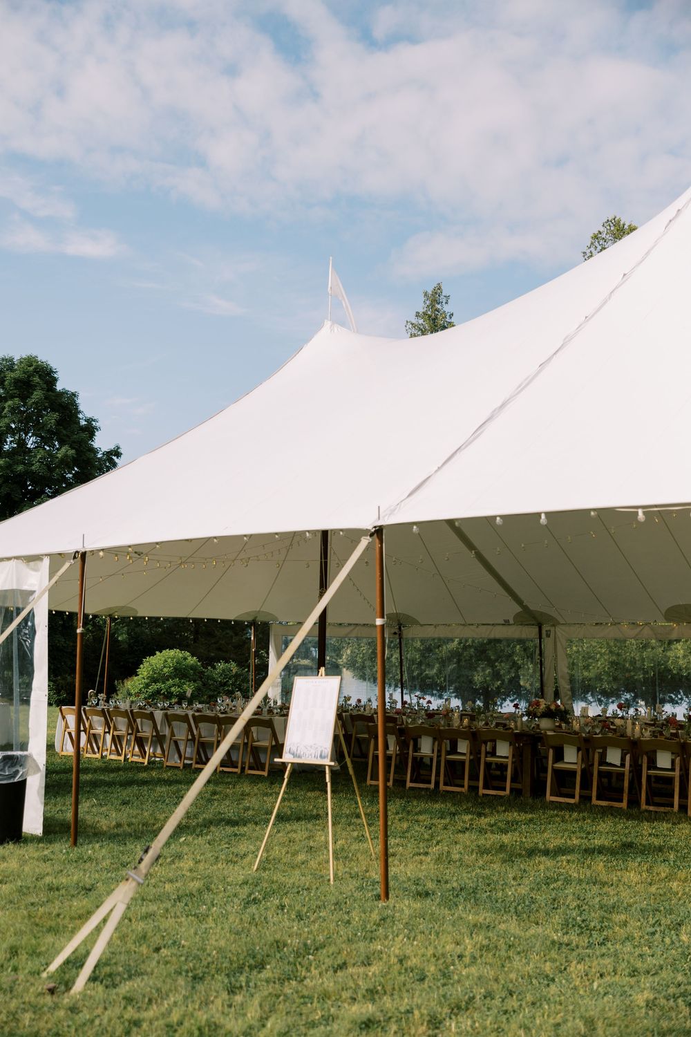 A white sailcloth wedding tent set up outdoors on grass with wooden folding chairs arranged underneath for a reception at Silver Bay YMCA.
