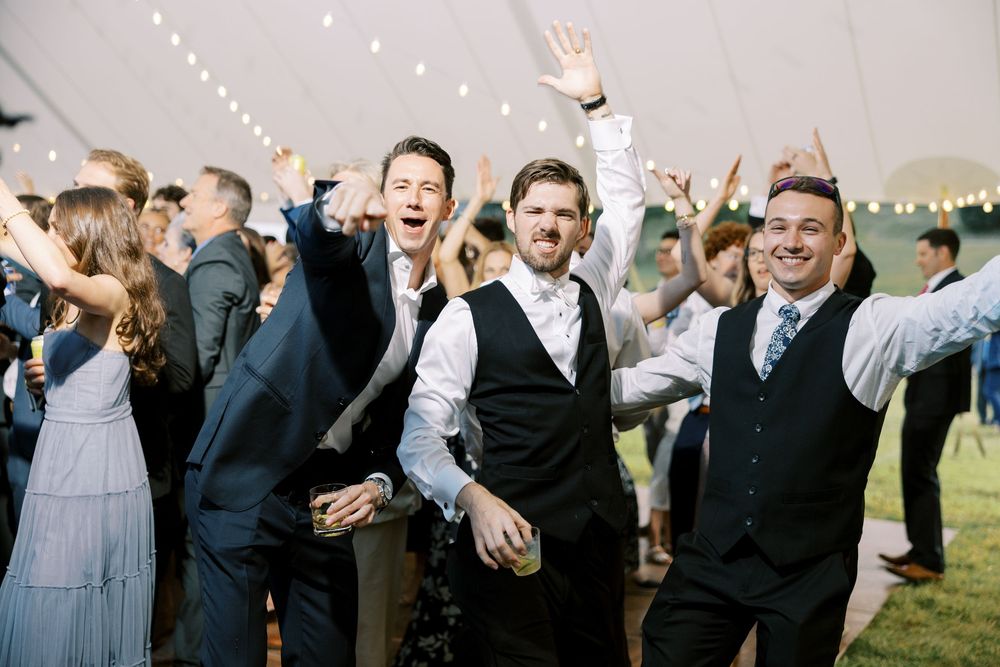 Wedding reception guests celebrate and dance together under string lights at an outdoor evening celebration.