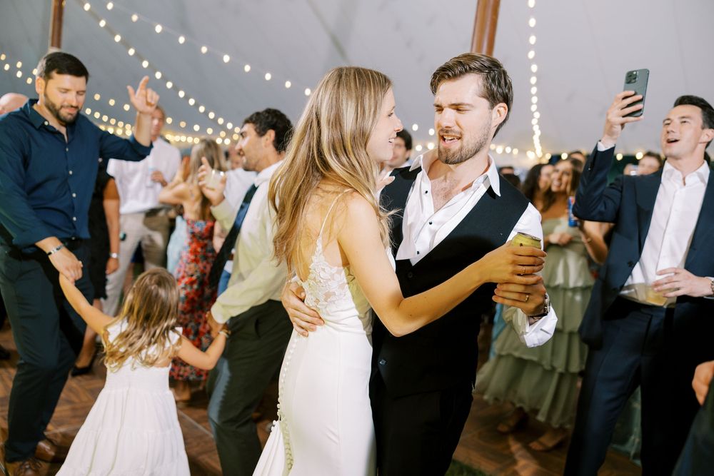 Wedding guests dancing and celebrating at a reception under string lights and elegant decor.
