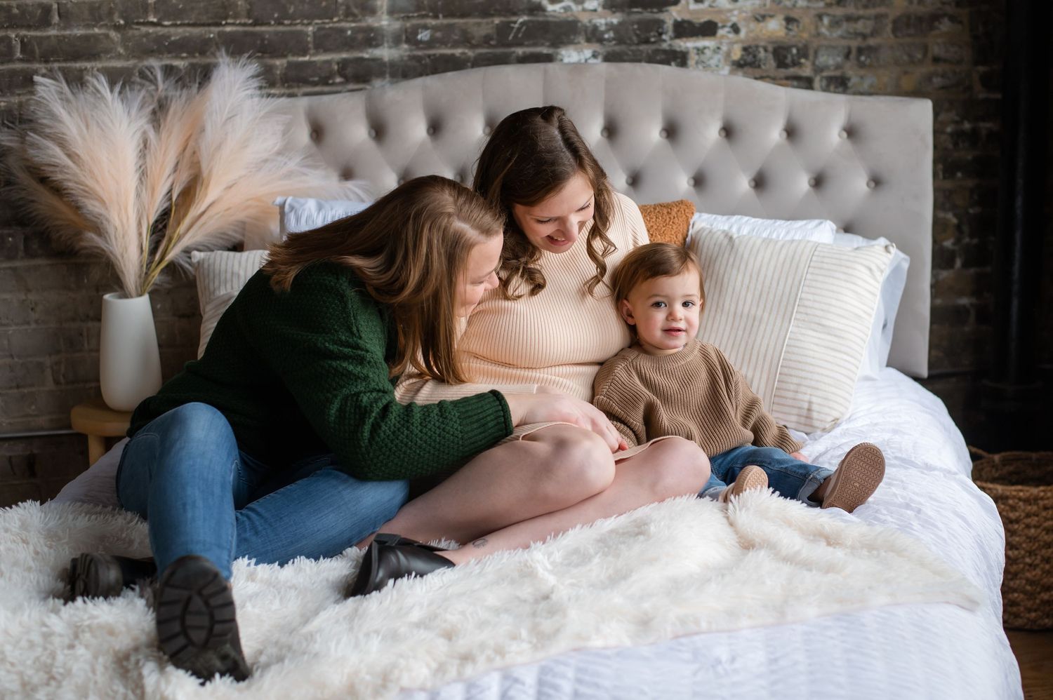 Cozy home scene with two people relaxing together on a plush gray couch with white bedding and decorative pampas grass.