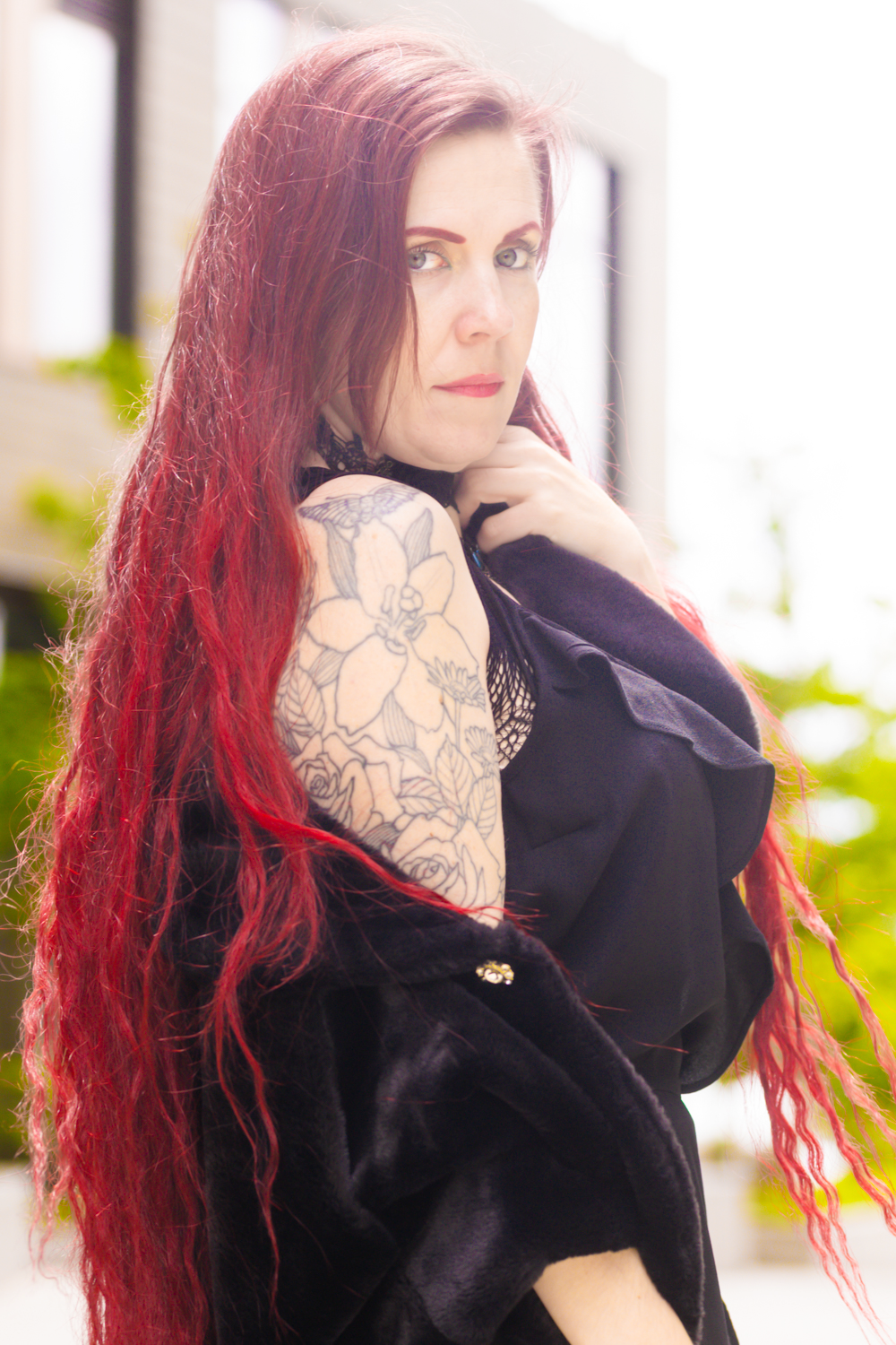 A gothic style portrait showing long red hair and black clothing with visible tattoo sleeve.