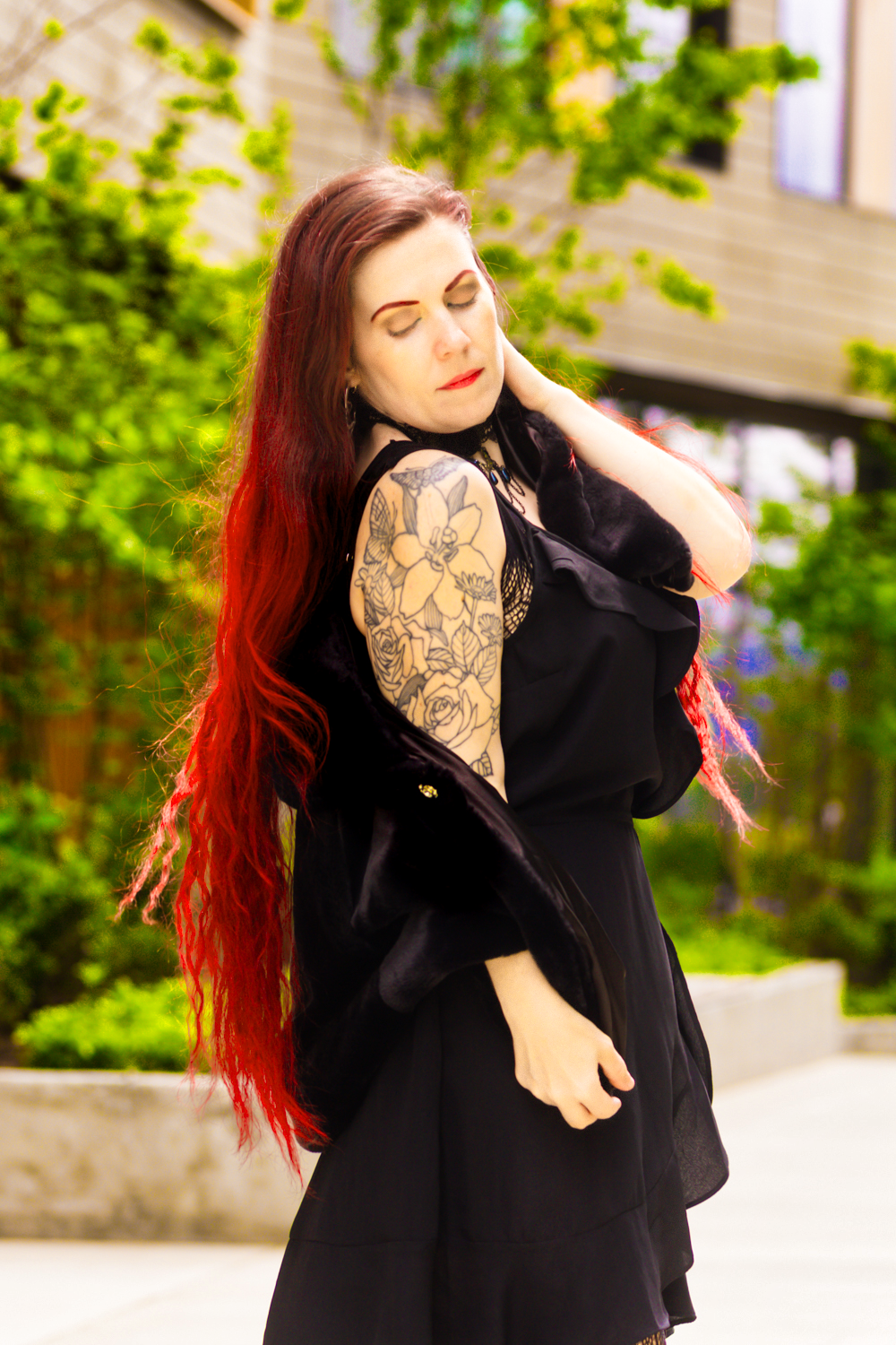 Artistic portrait showcasing vibrant red hair, a black dress, and an ornate sleeve tattoo in an outdoor setting.