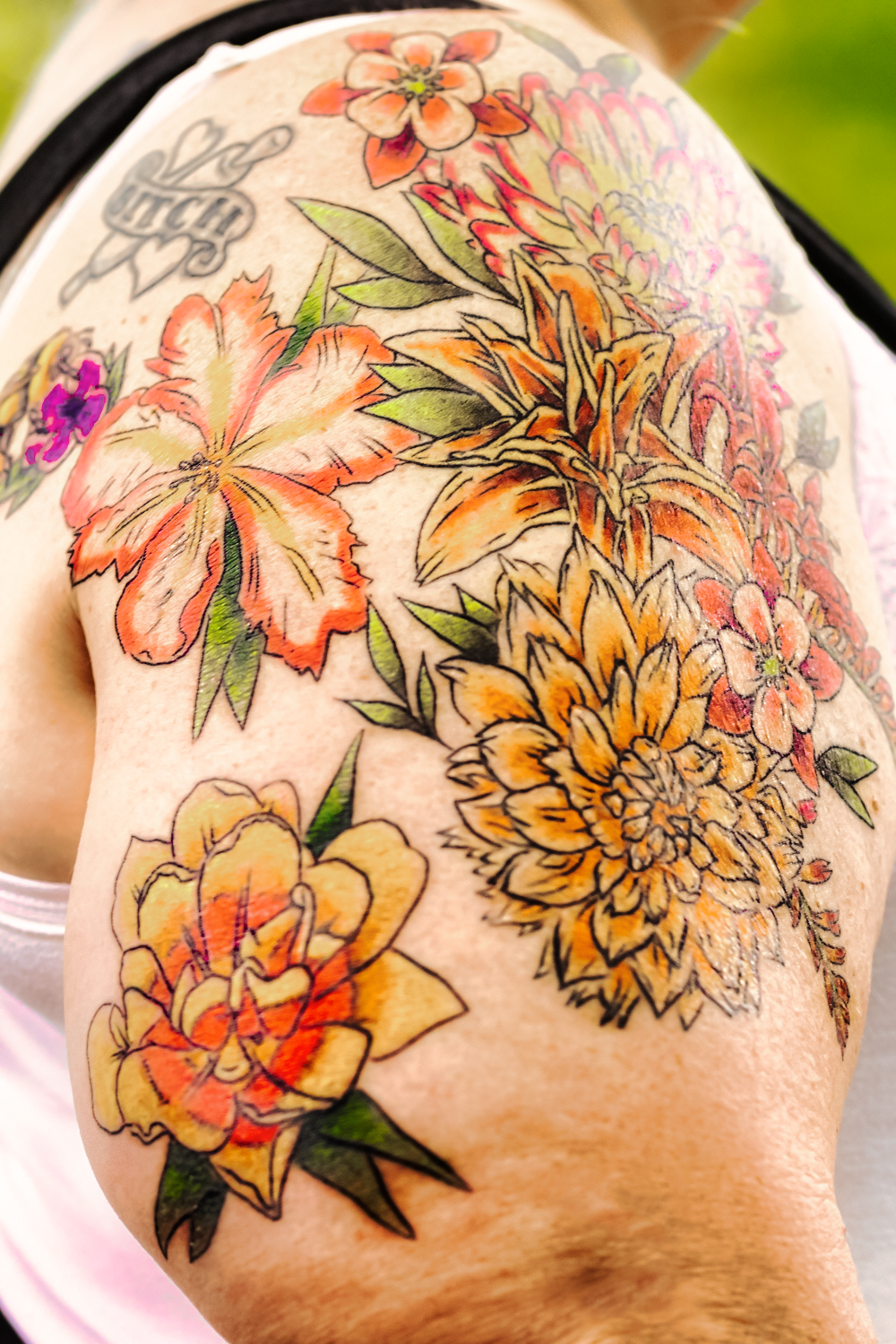 Colorful floral tattoo design featuring orange and yellow flowers with green leaves on skin.