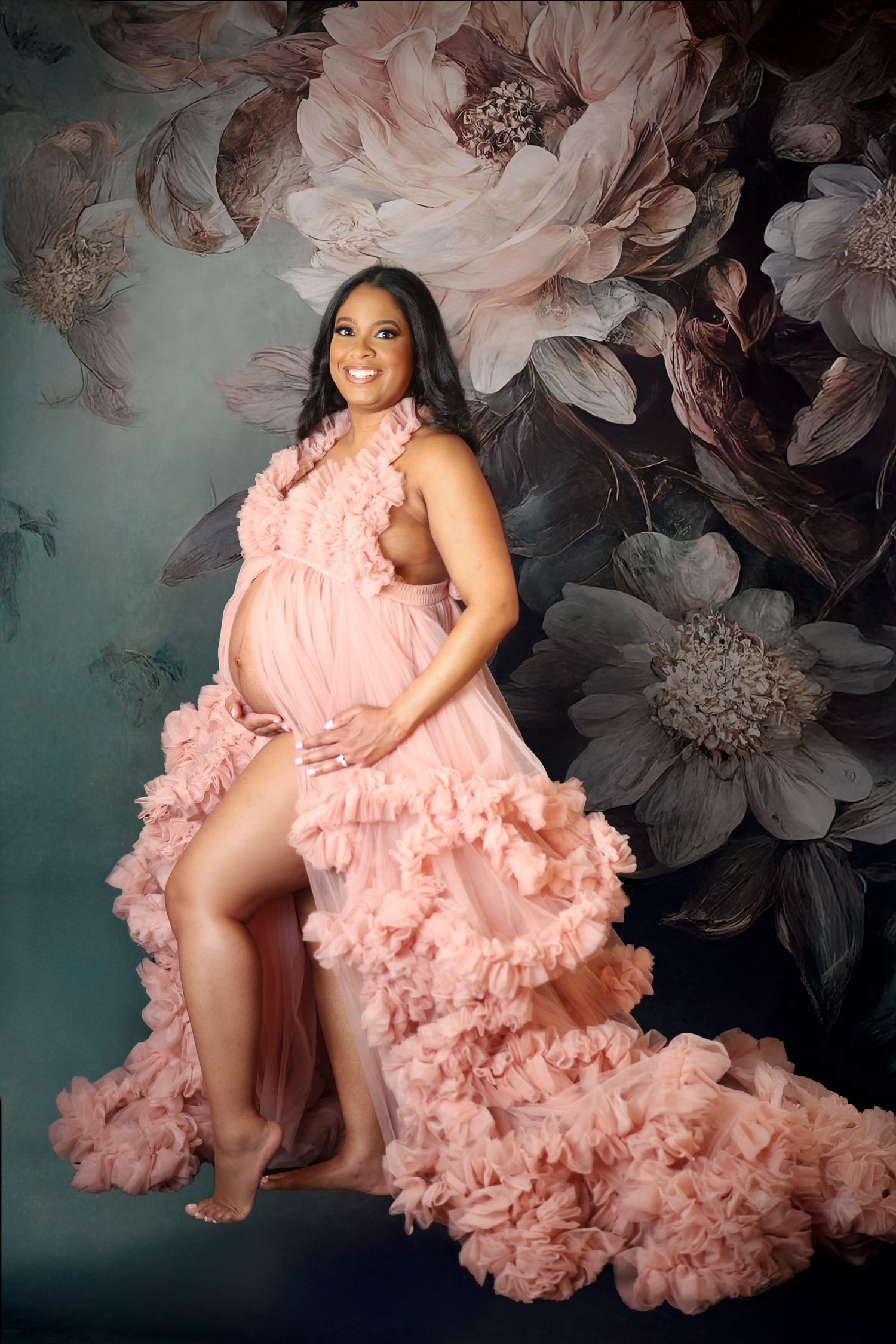 A Dallas pregnancy portrait against a floral backdrop featuring a flowing pink ruffled gown creating a dramatic, romantic effect.