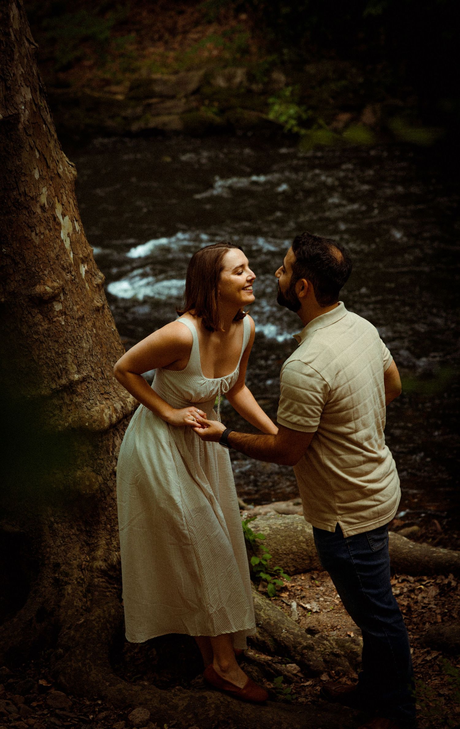 A couple shares a joyful moment together by a rushing stream in a wooded setting.