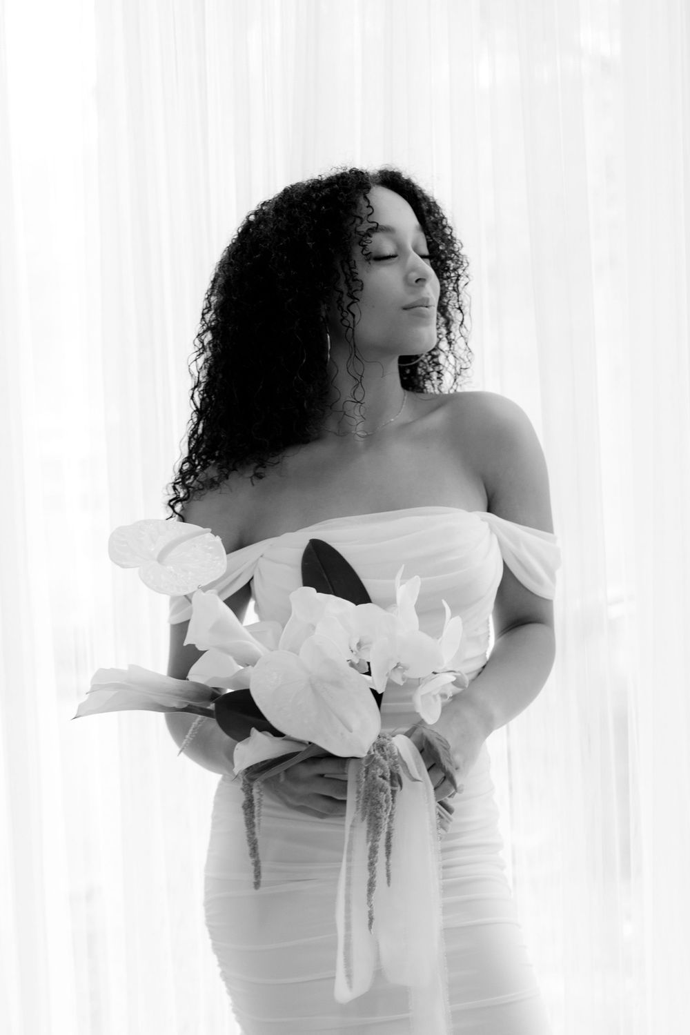 Elegant black and white portrait featuring a woman in an off-shoulder white dress holding a bouquet of flowers.