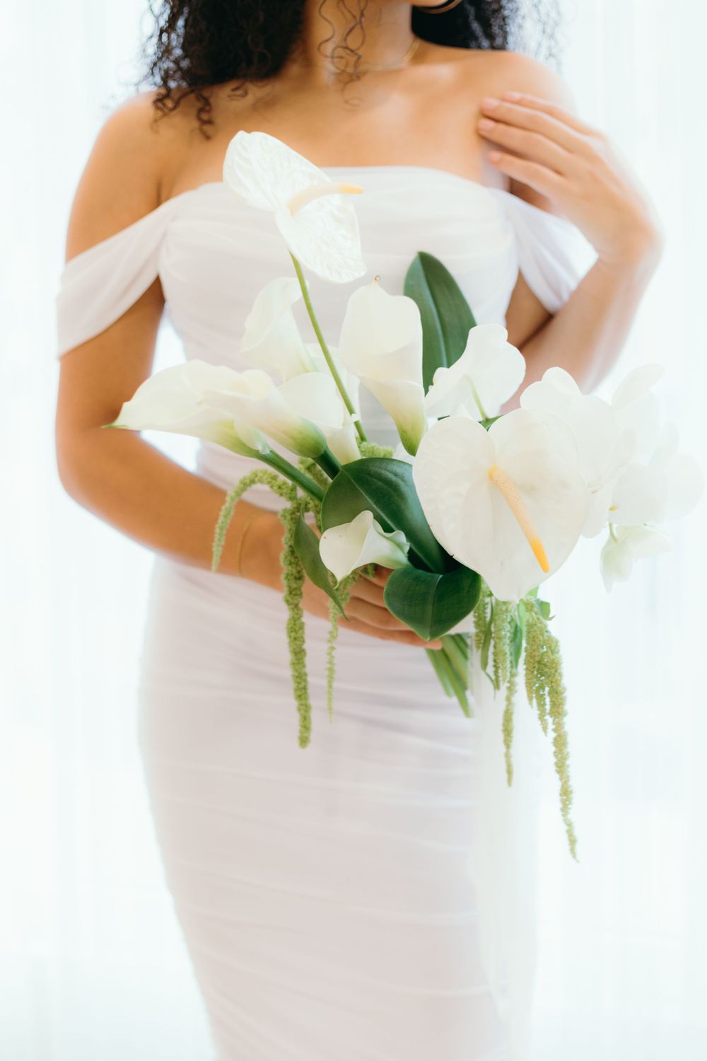 A white fitted wedding dress with an off-shoulder neckline paired with elegant white lily bouquet in minimalist style.