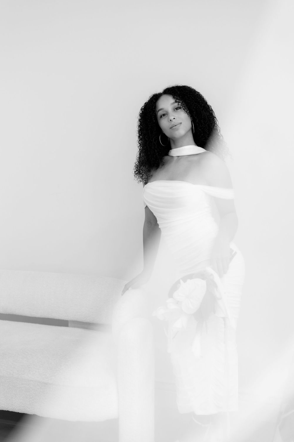 Artistic black and white fashion portrait of a woman in flowing white dress against minimalist background.
