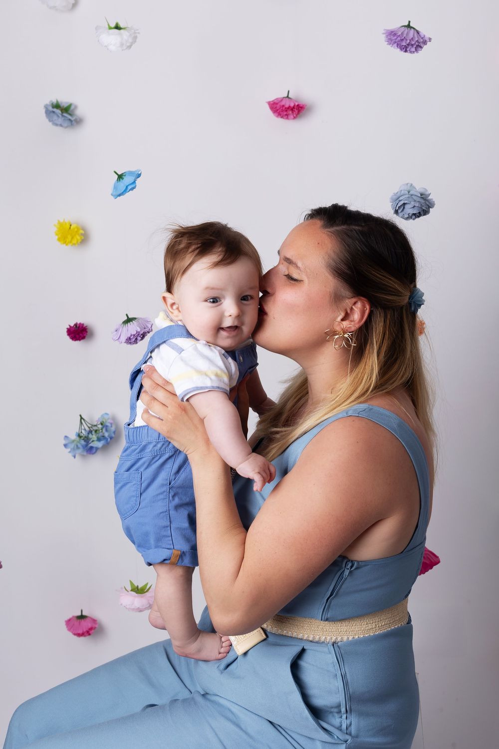 A tender moment against a white wall decorated with colorful paper flowers.