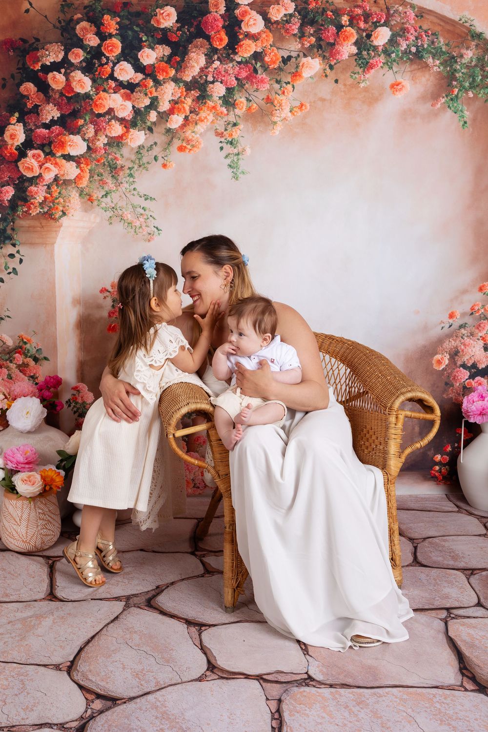 A tender moment in a floral arch setting with a wicker peacock chair and pink roses creating a romantic backdrop.
