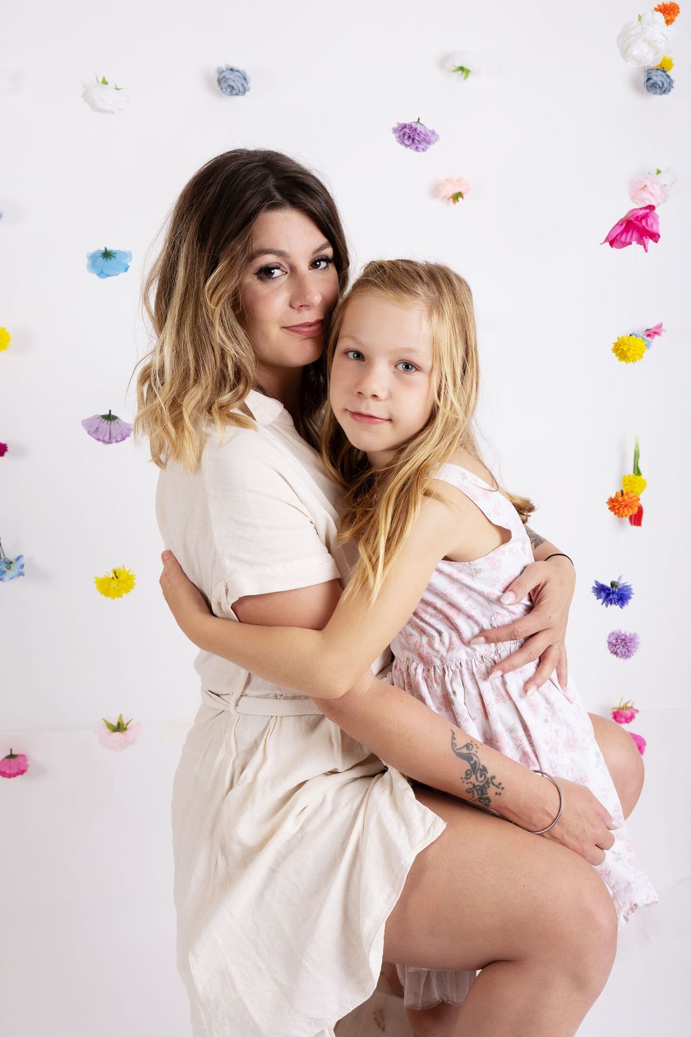 Two people hugging and posing against white background with colorful flower decorations.