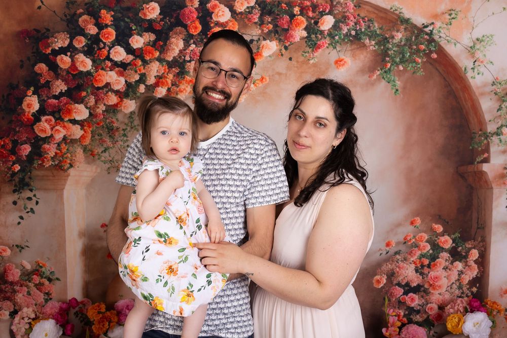 A family poses together against a romantic coral-colored backdrop with cascading peach flowers and floral decor.