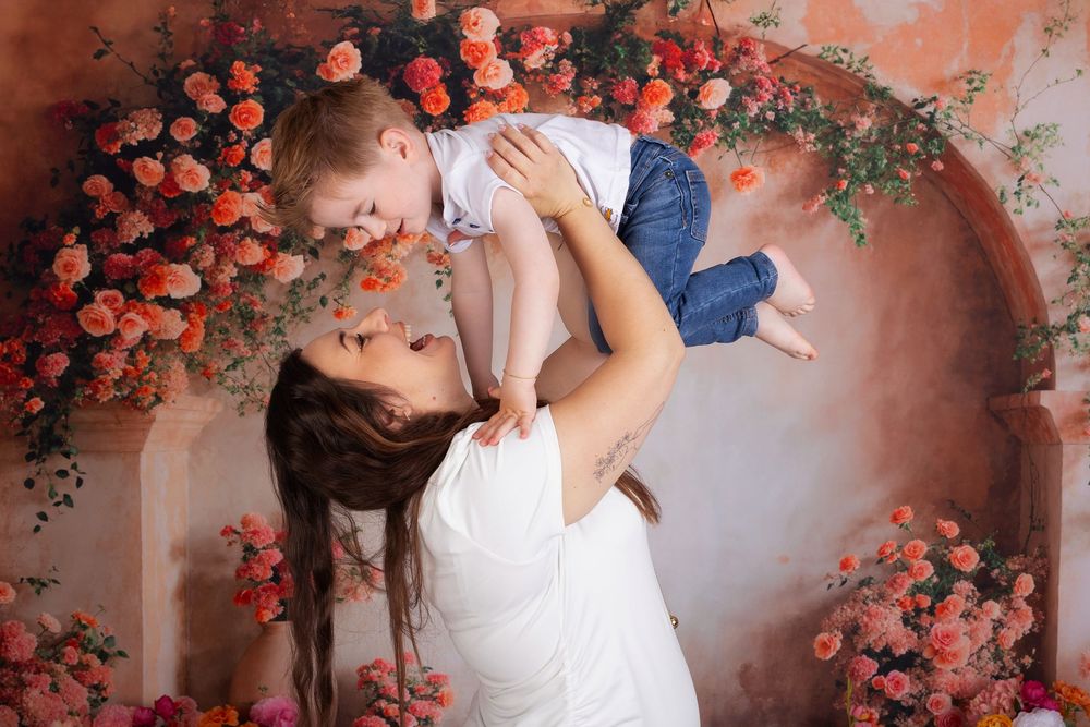 A loving moment captured against a romantic coral rose arch backdrop with soft lighting and delicate floral details.