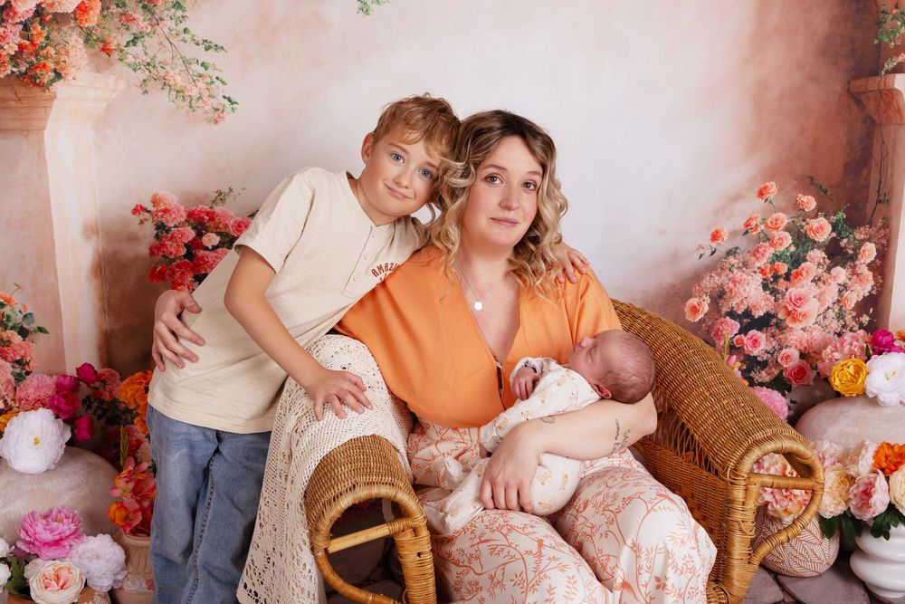 A family poses together in a floral studio setting with wicker furniture and pink roses surrounding them.