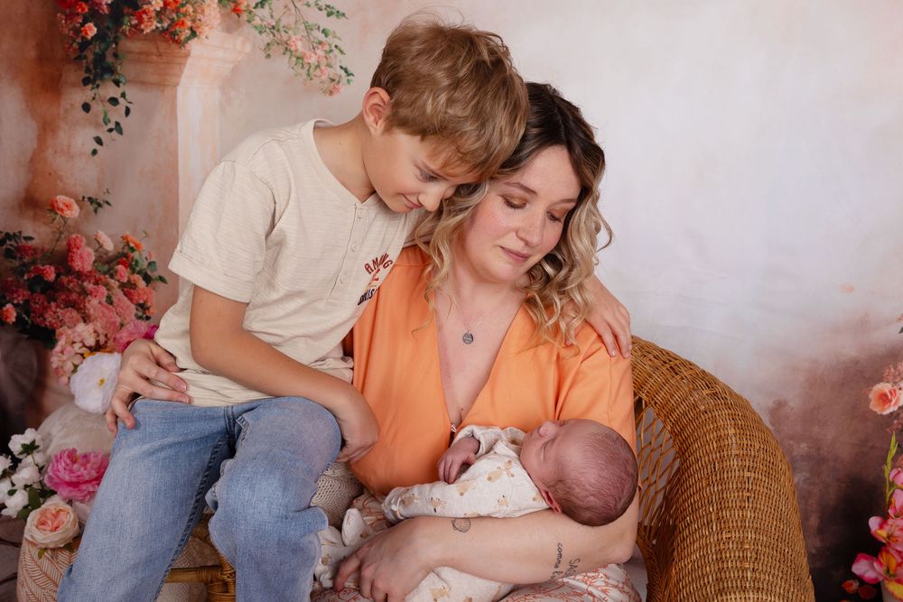 A tender family moment on a wicker chair surrounded by soft pink floral decorations in warm natural lighting.