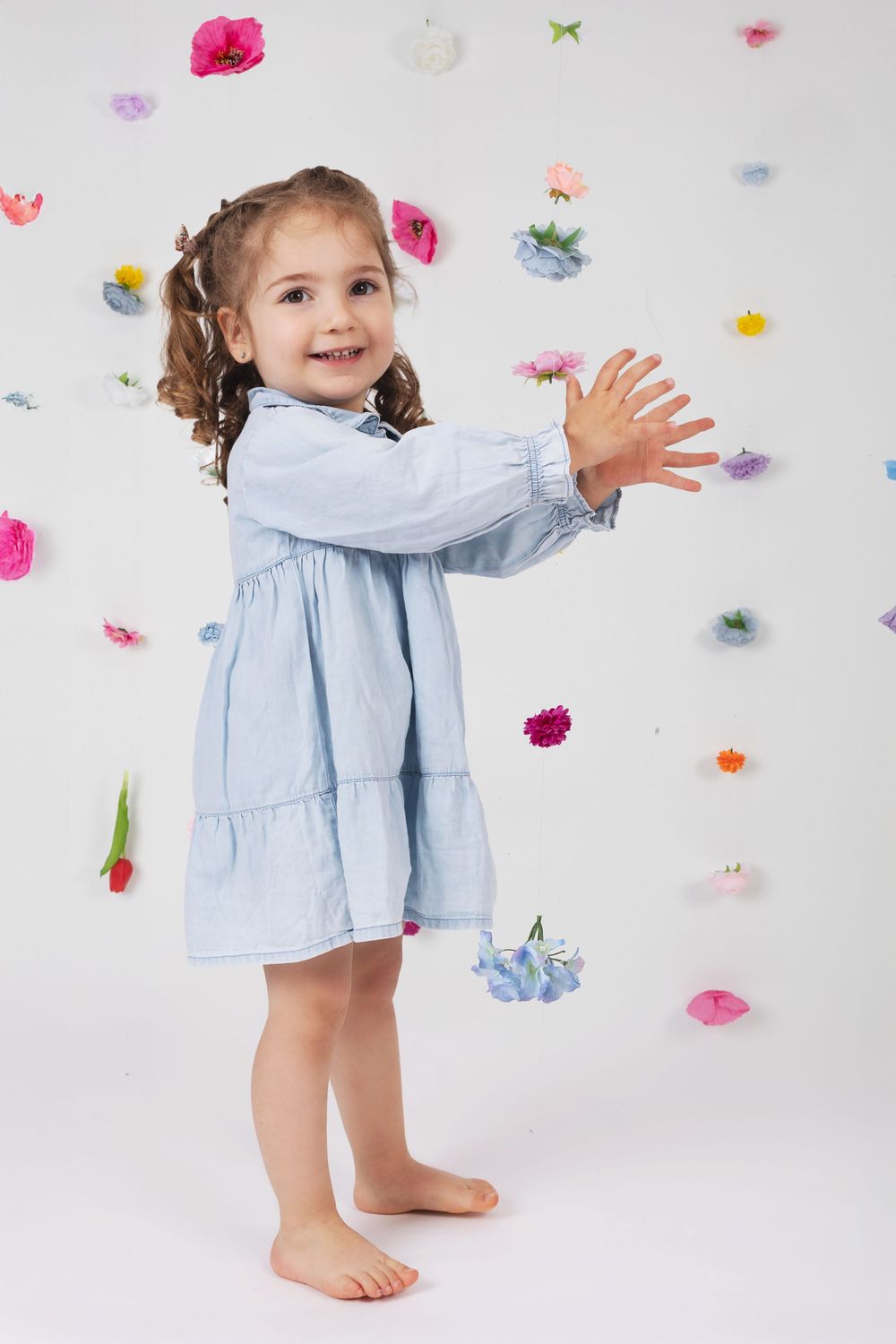 Sweet child in light blue dress plays against white background with colorful floral decorations.