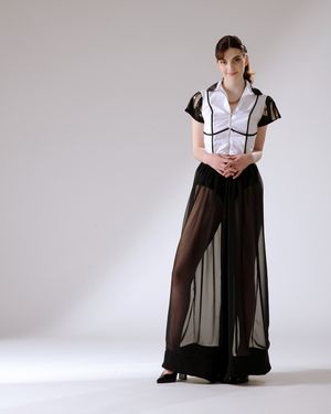 Model poses in black and white outfit with sheer palazzo pants against light gray studio backdrop.