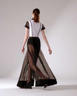 A model in a flowing sheer black palazzo pants and white top with black accents twirls against a light backdrop.