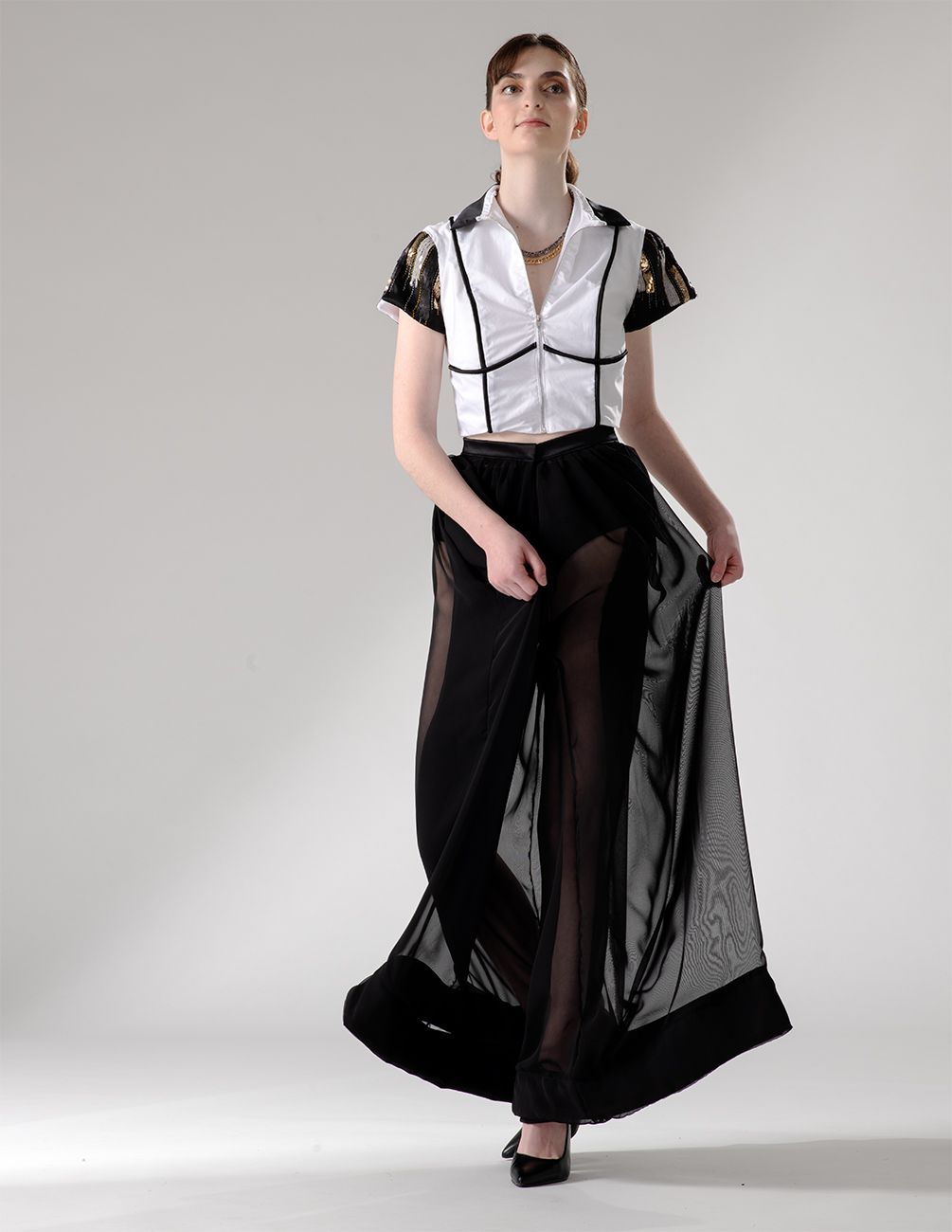Close-up fashion shot showing a contrasting white and black outfit with sheer overlay skirt against gray background.