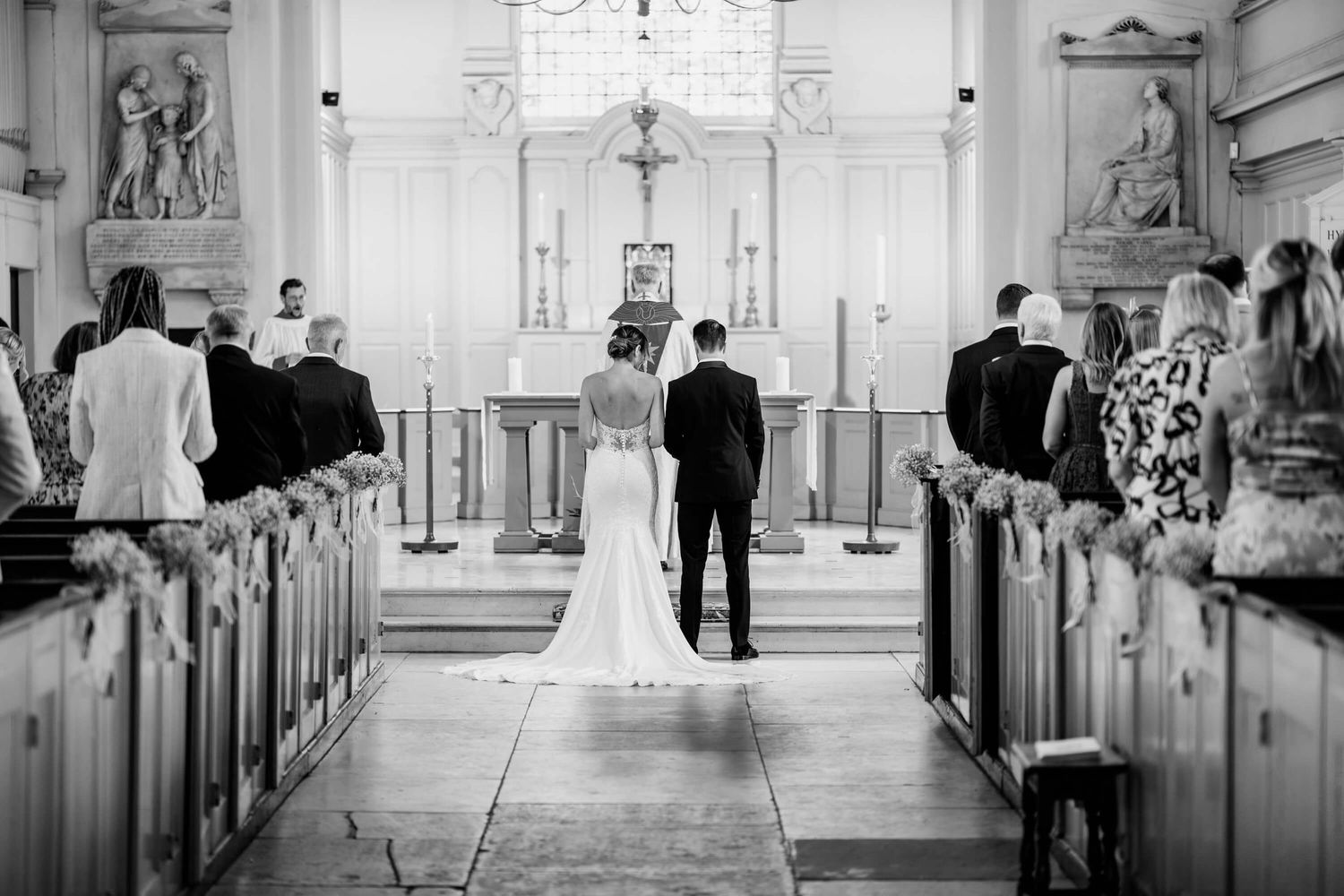 A black and white wedding ceremony photograph inside a church with guests seated in wooden pews.