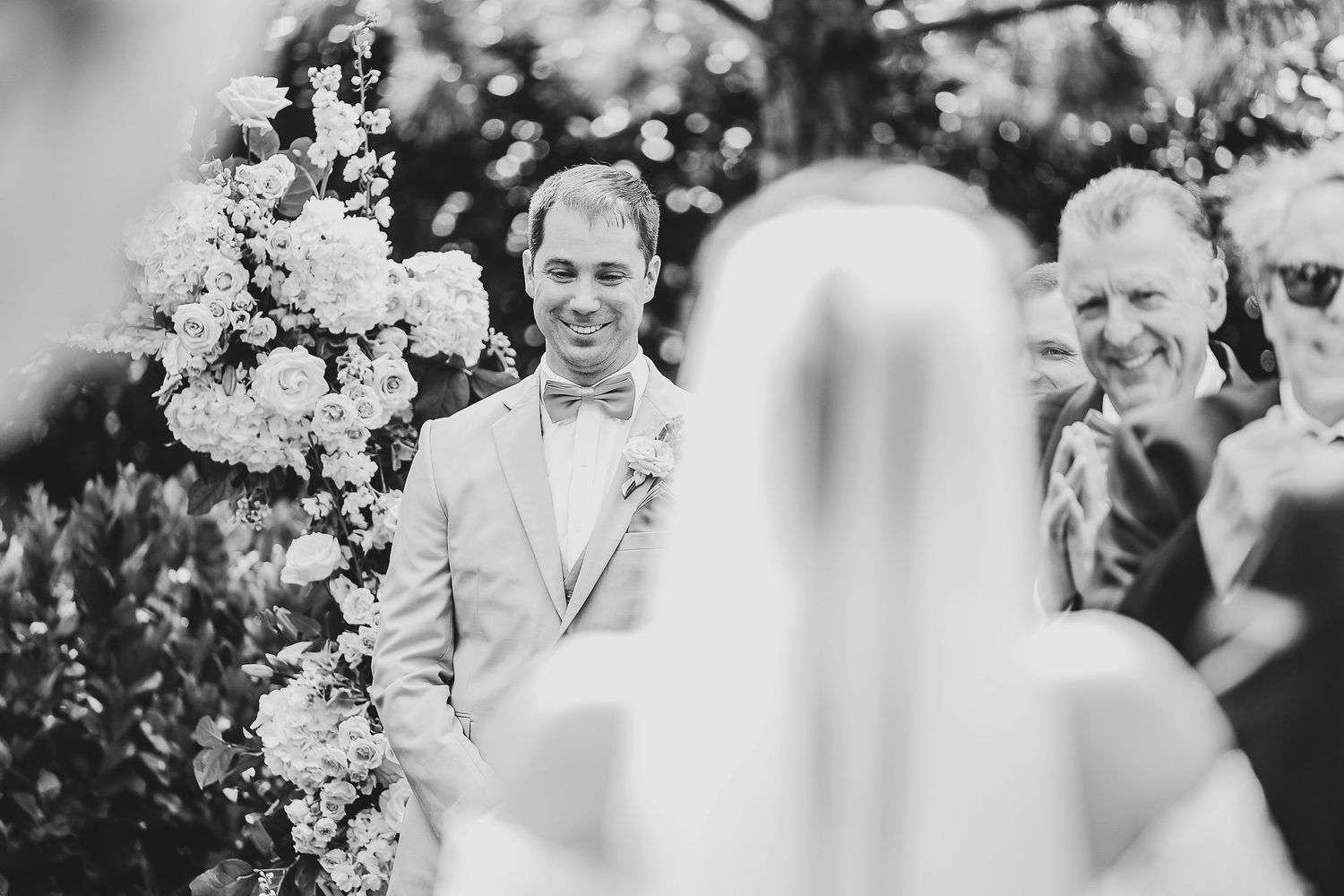 Groom in beige summer suit watching bride walk down the aisle