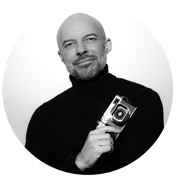 Professional black and white portrait of a photographer in a black turtleneck holding a vintage camera.