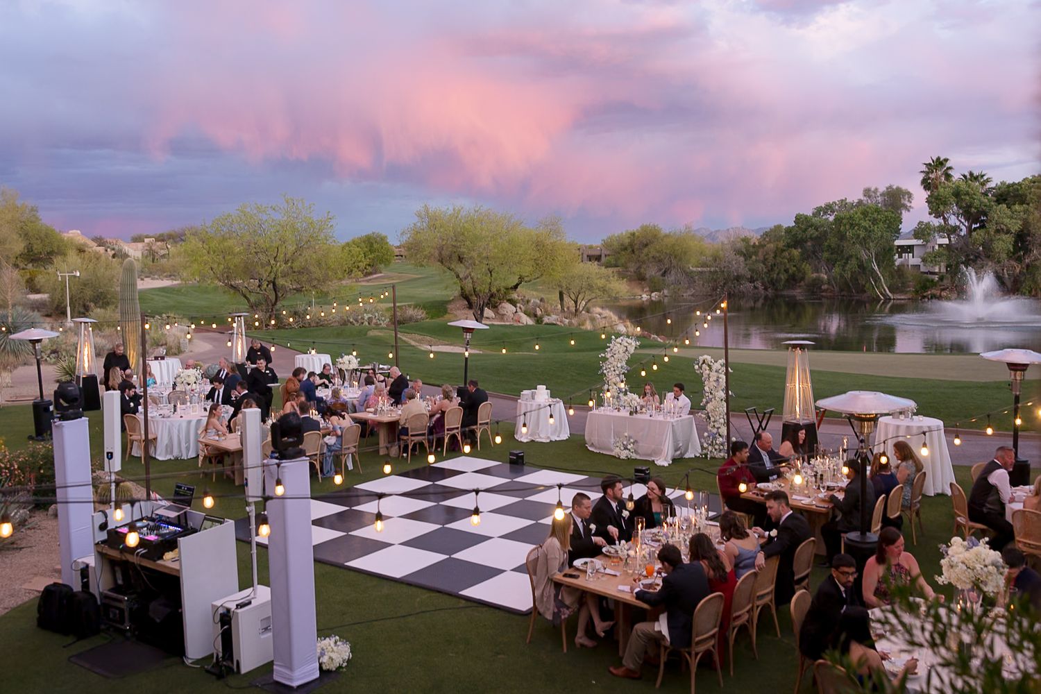 Rustic outdoor wedding venue features checkerboard dance floor and elegant table settings at sunset.