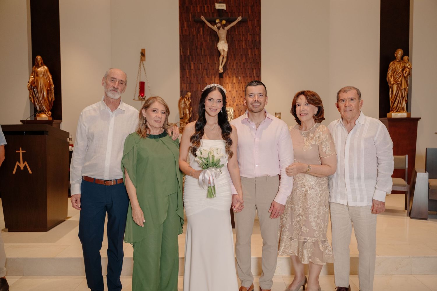 Wedding party poses together in a church sanctuary with wooden altar and religious statues in background.