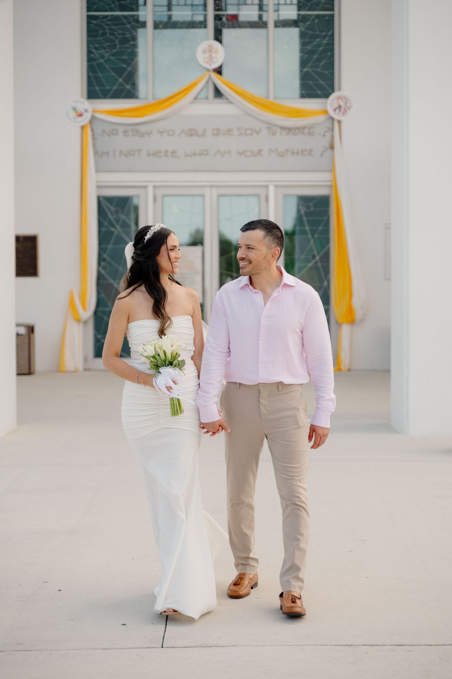 A couple shares a joyful moment at their wedding ceremony under a yellow and white draped arch.