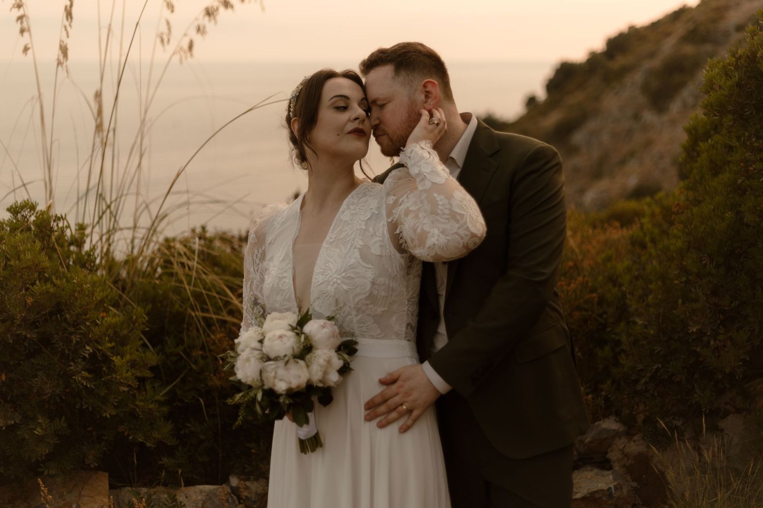 A romantic couple embraces during an outdoor photoshoot at golden hour with mountains in the background.