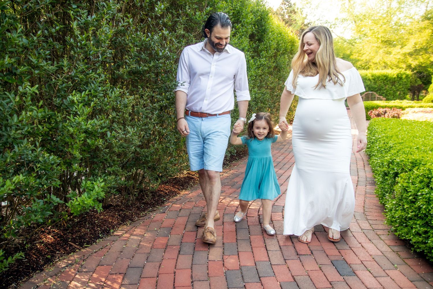 People walking together on a winding brick pathway surrounded by lush greenery on a sunny day.